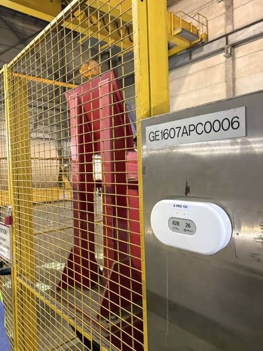 Capteur de qualité de l'air fixé sur une machine d'atelier, derrière une grille de protection jaune