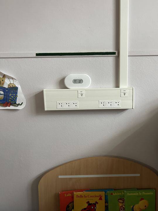 Capteur de qualité de l'air fixé au mur d'une salle de crèche, au-dessus d'un bac à livres