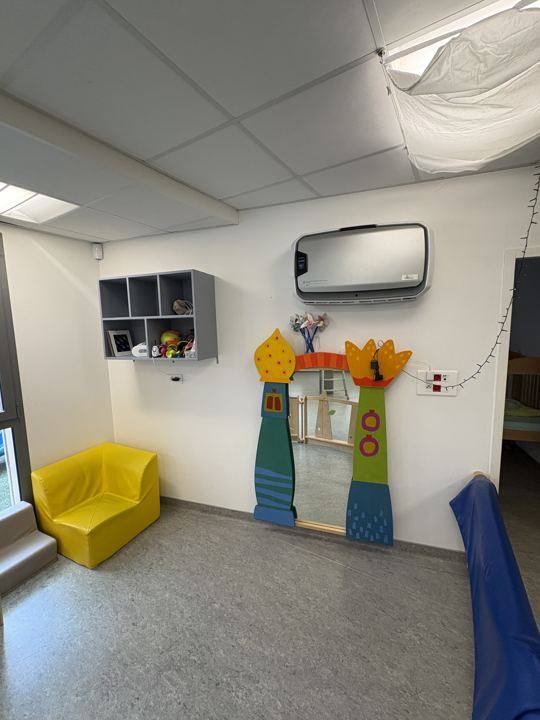 Purificateur d'air fixé au mur d'une salle de crèche, près d'un fauteuil jaune